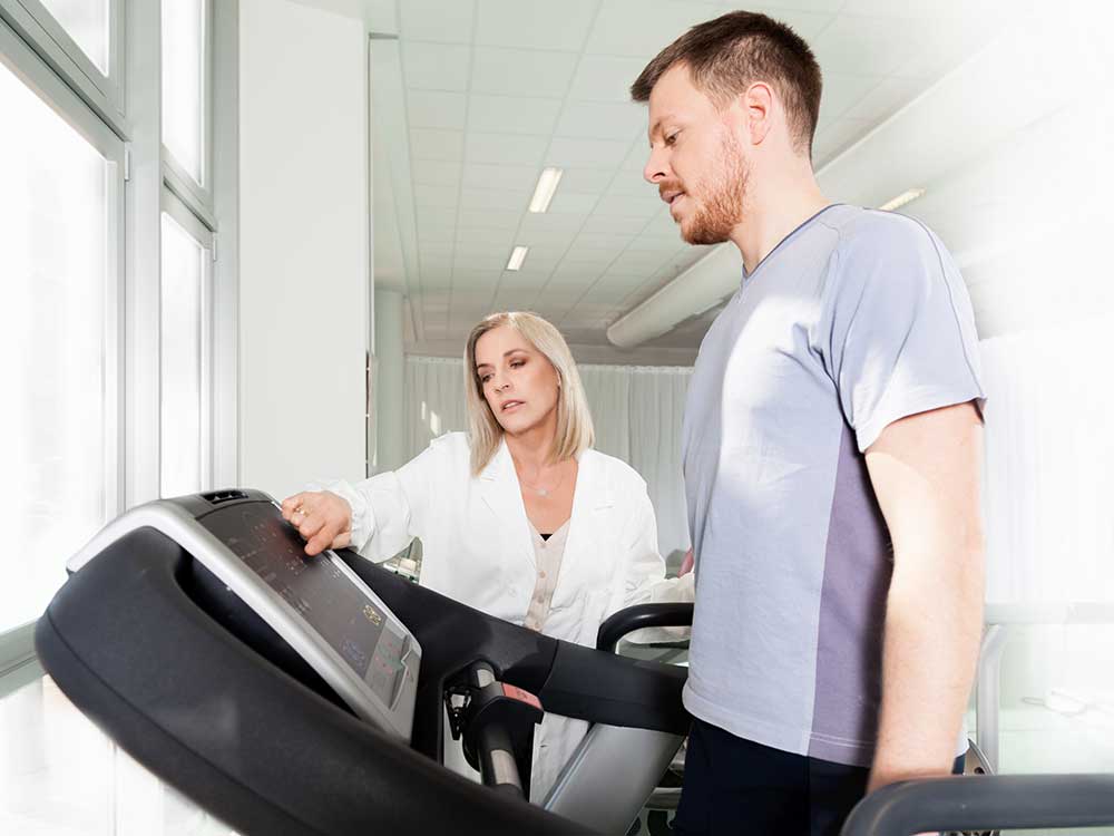 Client on a treadmill; medical evaluator checks settings.
